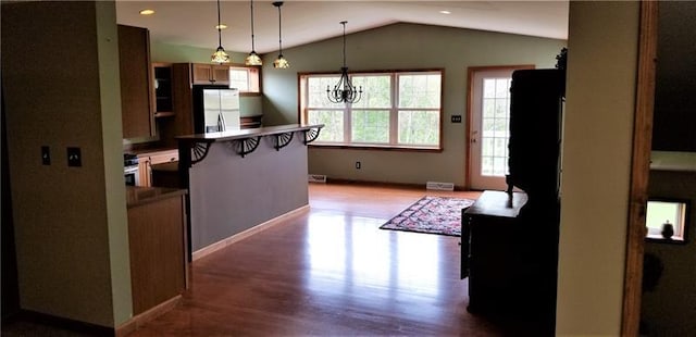 kitchen featuring stainless steel fridge, vaulted ceiling, a kitchen bar, a notable chandelier, and hardwood / wood-style flooring