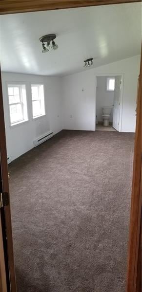 empty room with baseboard heating, dark colored carpet, and vaulted ceiling