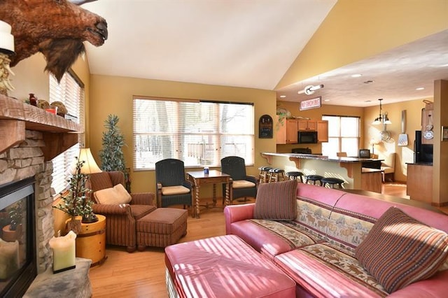 living room featuring an inviting chandelier, a stone fireplace, high vaulted ceiling, and light wood-type flooring