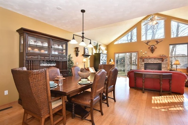 dining area with high vaulted ceiling, light hardwood / wood-style flooring, a healthy amount of sunlight, and a stone fireplace