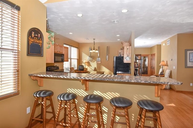 kitchen featuring kitchen peninsula, black appliances, a breakfast bar area, and light wood-type flooring