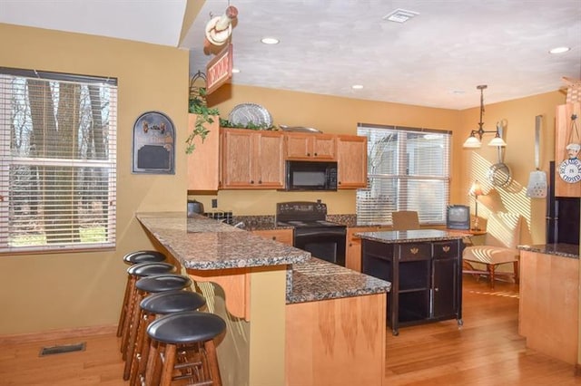 kitchen featuring a kitchen breakfast bar, decorative light fixtures, kitchen peninsula, light hardwood / wood-style flooring, and range