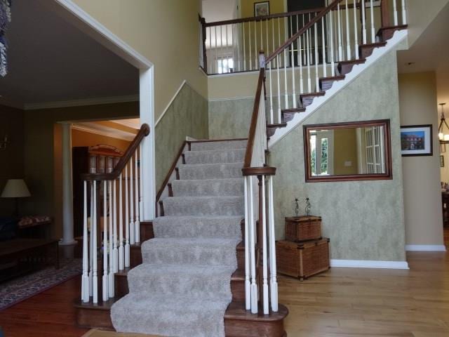 staircase with a towering ceiling, crown molding, and hardwood / wood-style flooring