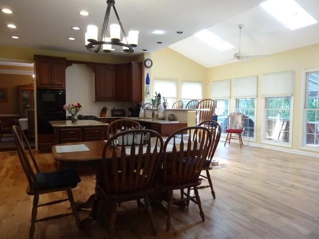 dining room with an inviting chandelier, sink, light hardwood / wood-style floors, and lofted ceiling with skylight