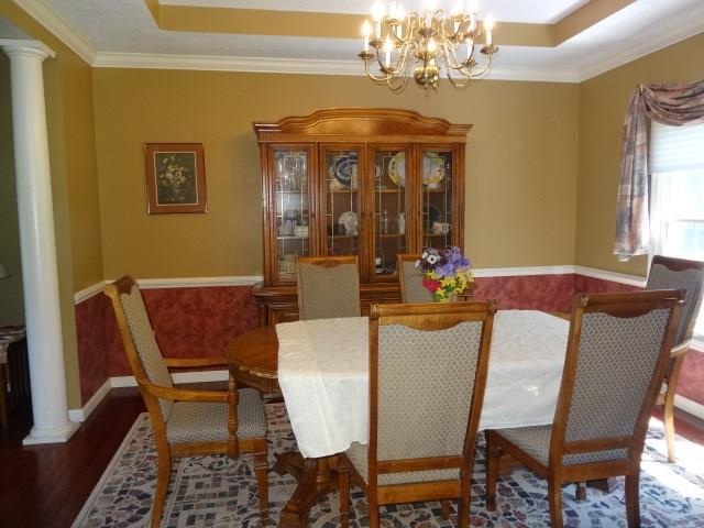 dining area featuring a tray ceiling, dark wood-type flooring, a notable chandelier, and ornate columns