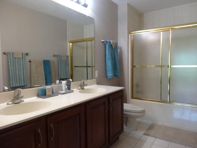 full bathroom with combined bath / shower with glass door, double sink vanity, tile floors, and toilet