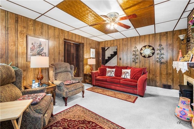 carpeted living room featuring a drop ceiling, ceiling fan, and wood walls