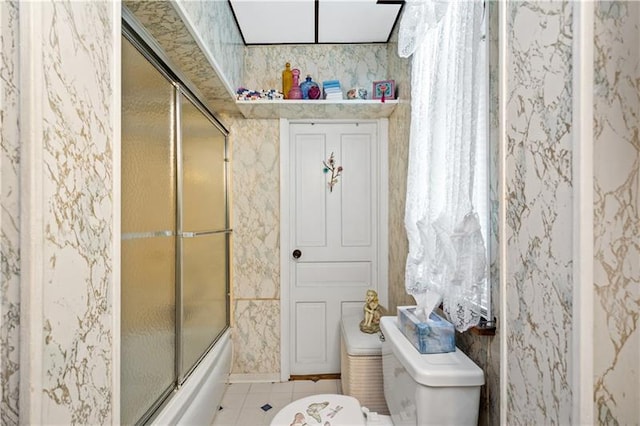 bathroom featuring tile flooring, toilet, and bath / shower combo with glass door