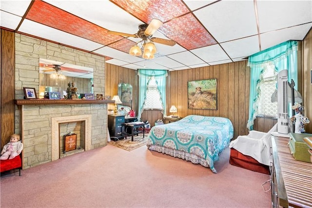 bedroom with a fireplace, ceiling fan, wooden walls, and multiple windows