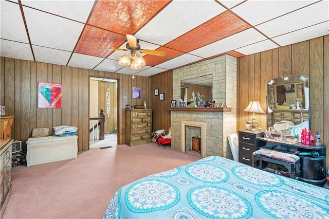 carpeted bedroom with a fireplace, wood walls, ceiling fan, and a paneled ceiling