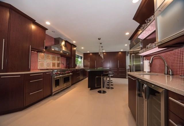 kitchen with hanging light fixtures, a breakfast bar area, premium appliances, wall chimney range hood, and sink