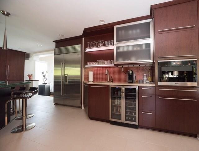 bar with black oven, light tile flooring, beverage cooler, tasteful backsplash, and stainless steel built in fridge