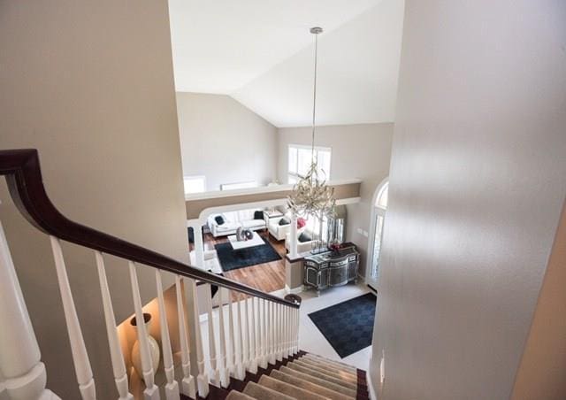 stairs with an inviting chandelier, wood-type flooring, and lofted ceiling