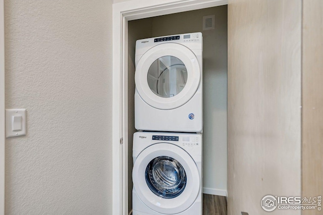 clothes washing area featuring stacked washer and dryer and wood-type flooring