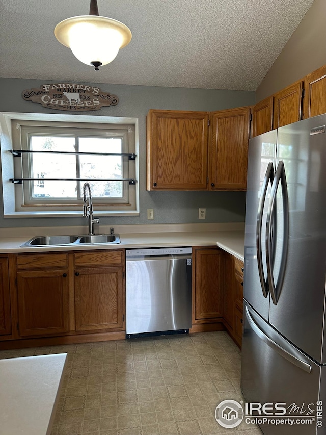 kitchen featuring sink, stainless steel appliances, hanging light fixtures, and a textured ceiling