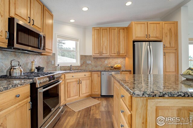 kitchen featuring dark stone counters, a sink, ornamental molding, stainless steel appliances, and light wood-style floors