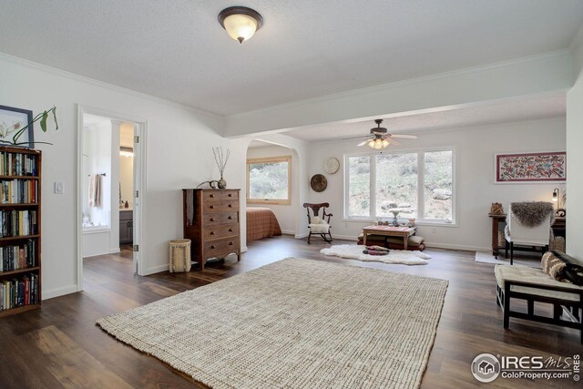 sitting room featuring dark wood-style floors, arched walkways, crown molding, baseboards, and ceiling fan