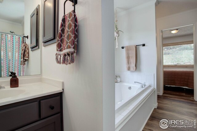 full bath featuring vanity, crown molding, a garden tub, and wood finished floors