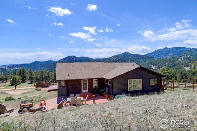 view of front facade with a mountain view, a shingled roof, a patio, and fence