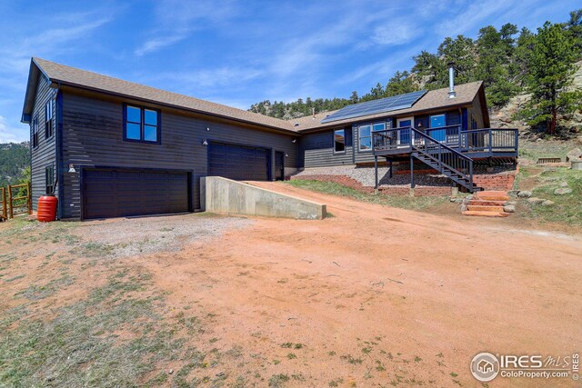 view of front facade featuring solar panels, stairway, dirt driveway, and a wooden deck