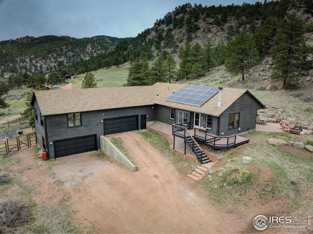 view of front of property with a deck with mountain view, driveway, fence, a shingled roof, and solar panels