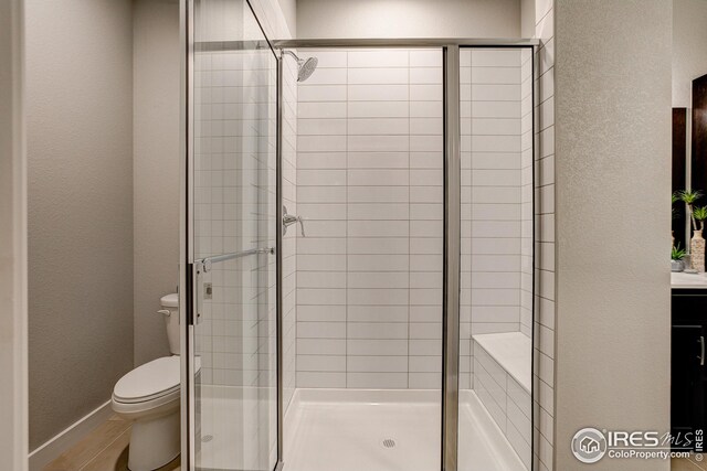 bathroom featuring a shower with door, vanity, and toilet