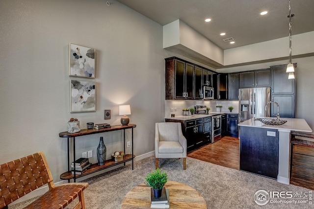 kitchen featuring pendant lighting, an island with sink, wood-type flooring, appliances with stainless steel finishes, and decorative backsplash