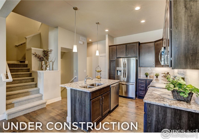 kitchen featuring backsplash, appliances with stainless steel finishes, light stone countertops, sink, and a kitchen island with sink