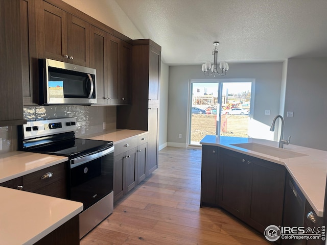 kitchen featuring sink, hanging light fixtures, stainless steel appliances, light hardwood / wood-style flooring, and a notable chandelier