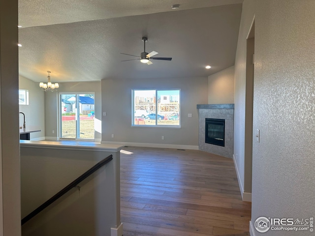 unfurnished living room with hardwood / wood-style flooring, plenty of natural light, ceiling fan with notable chandelier, and a tiled fireplace