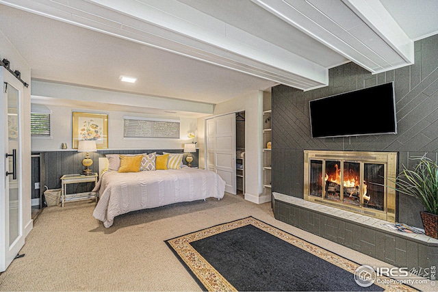 bedroom featuring a tiled fireplace, a barn door, carpet, and beam ceiling