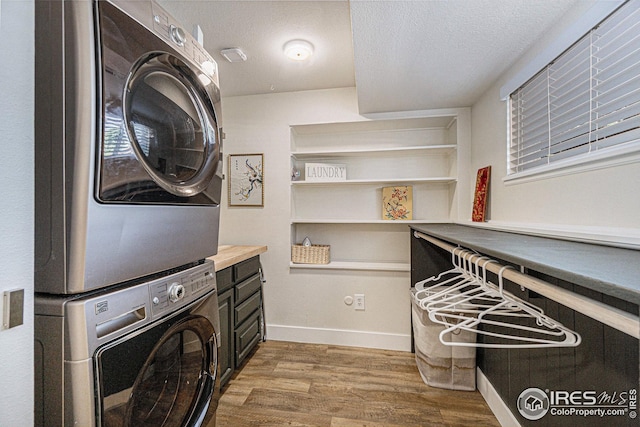 laundry room with stacked washer and clothes dryer, light wood-style flooring, a textured ceiling, laundry area, and baseboards