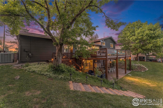 back of property at dusk with a deck, a patio, central AC unit, stairway, and a lawn