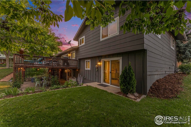 back of property with a lawn, a patio, stairs, a wooden deck, and board and batten siding