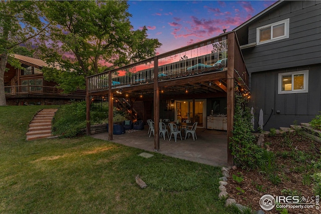 back of house at dusk featuring a patio area, stairway, a lawn, and board and batten siding