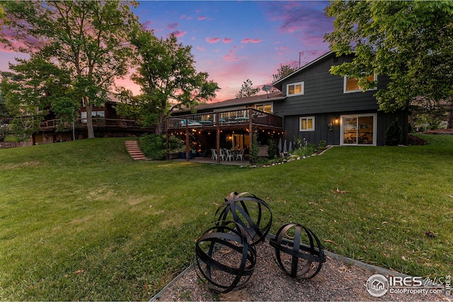 back of house at dusk with a patio, a lawn, a deck, and stairs