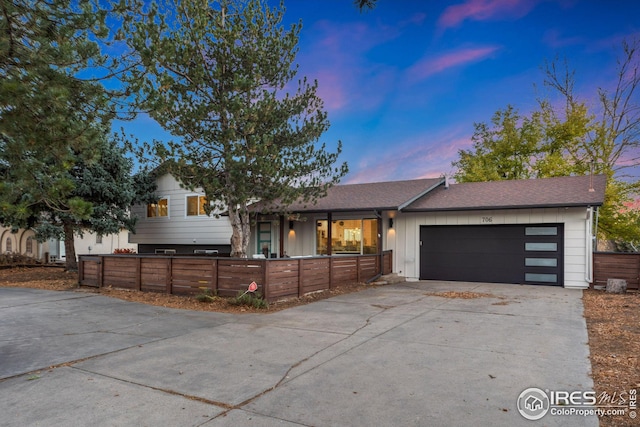 split level home with a fenced front yard, a garage, a shingled roof, concrete driveway, and board and batten siding