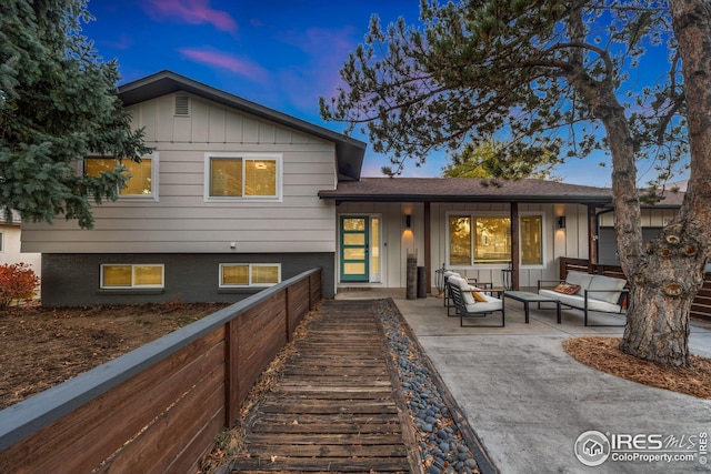 back of house at dusk featuring outdoor lounge area, board and batten siding, and brick siding