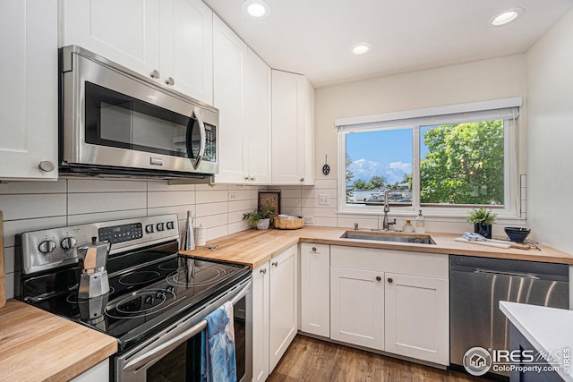 kitchen with stainless steel appliances, decorative backsplash, white cabinets, a sink, and wood counters