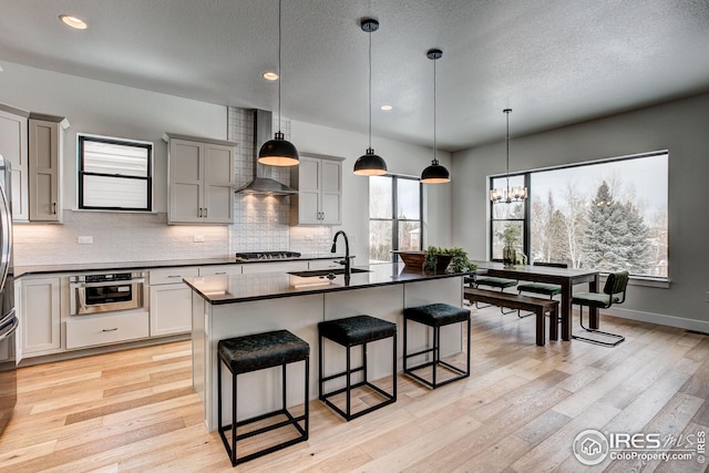 kitchen featuring tasteful backsplash, sink, pendant lighting, light wood-type flooring, and wall chimney exhaust hood