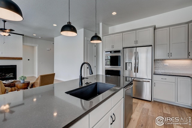 kitchen with light hardwood / wood-style flooring, stainless steel appliances, a fireplace, hanging light fixtures, and decorative backsplash