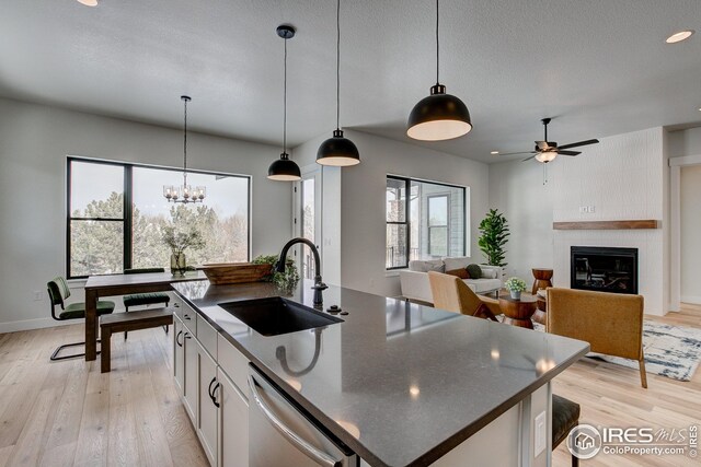 kitchen featuring sink, a fireplace, stainless steel dishwasher, a kitchen island with sink, and light wood-type flooring