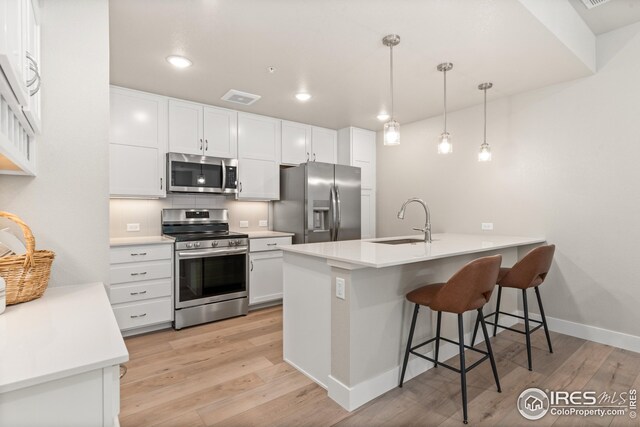 kitchen featuring stainless steel appliances, light hardwood / wood-style floors, white cabinetry, and hanging light fixtures