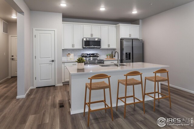 kitchen with appliances with stainless steel finishes, sink, an island with sink, dark hardwood / wood-style flooring, and white cabinets