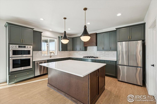 kitchen featuring light wood-type flooring, stainless steel appliances, sink, decorative light fixtures, and a center island