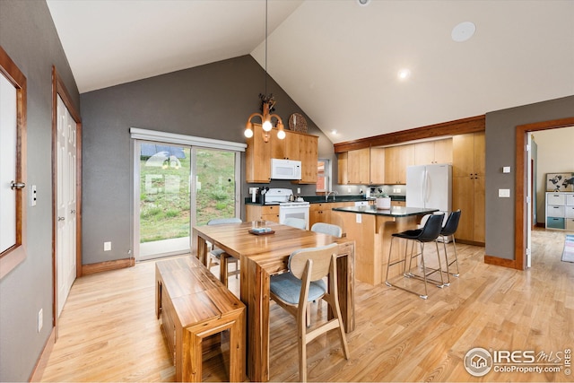 dining room with an inviting chandelier, high vaulted ceiling, sink, and light hardwood / wood-style flooring