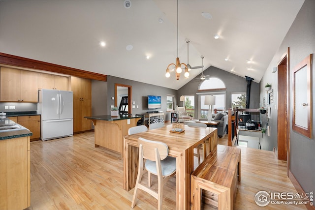 dining room with an inviting chandelier, high vaulted ceiling, light wood-type flooring, and a wood stove