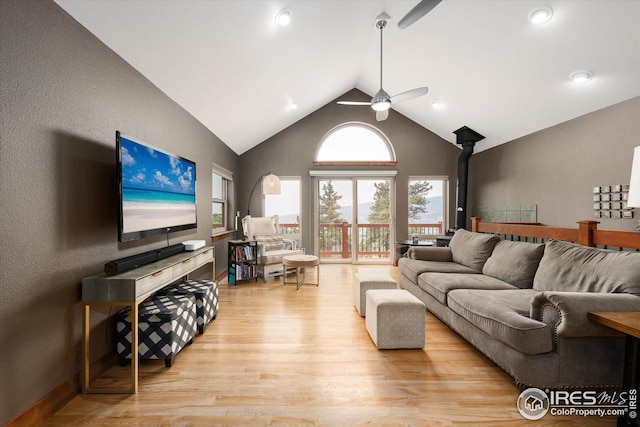 living room featuring a wood stove, high vaulted ceiling, ceiling fan, and light wood-type flooring