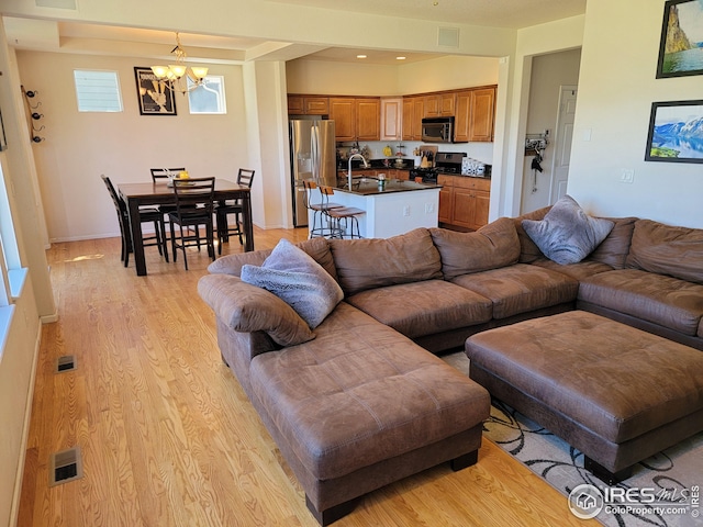 living room with a notable chandelier, sink, and light hardwood / wood-style flooring