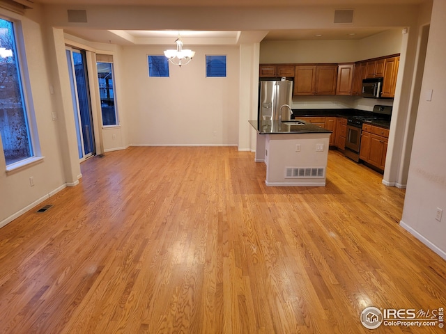 kitchen with appliances with stainless steel finishes, a kitchen island with sink, decorative light fixtures, a chandelier, and light hardwood / wood-style floors